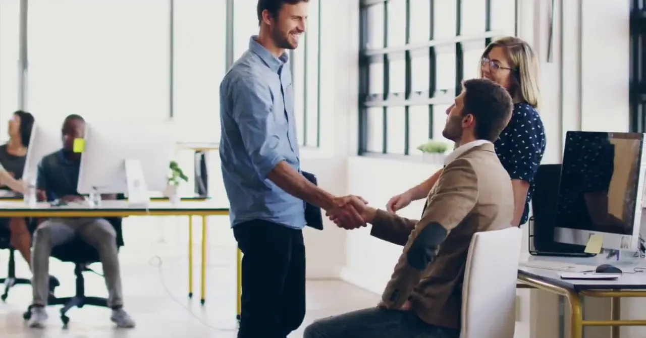 A handshake between colleagues in a bright open-plan office