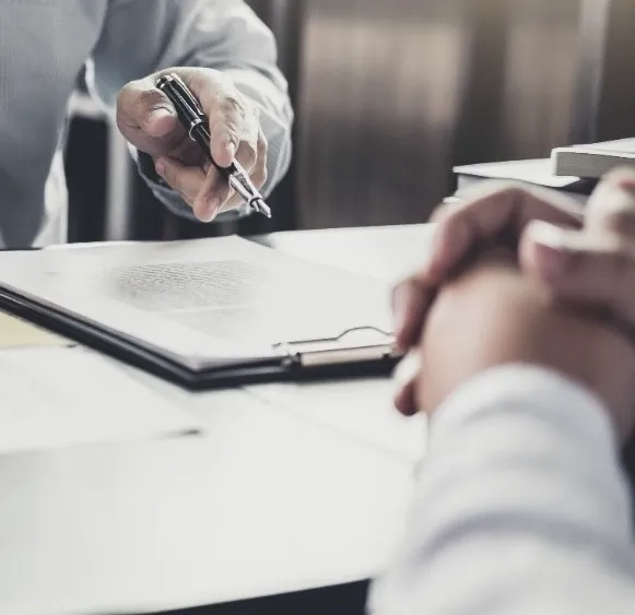 A client with clasped hands listening to a solicitor across a desk